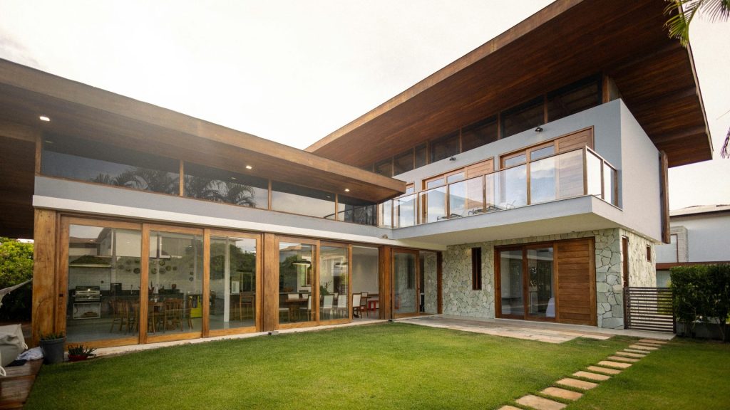Modernes Luxushaus mit großer Glasfensterfront, Holzdekor und grünem Rasen.