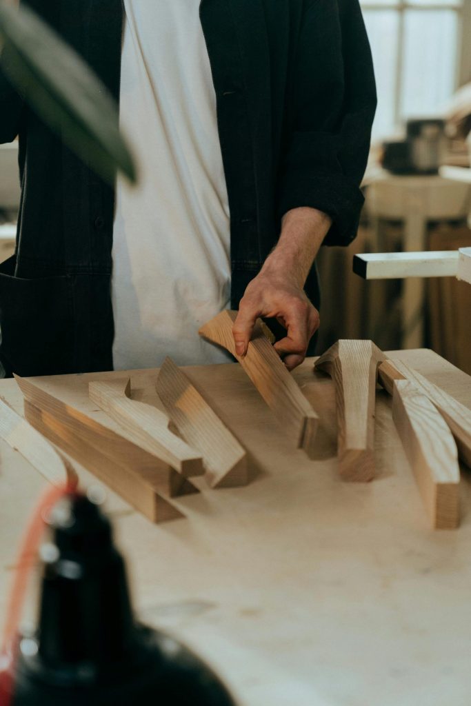 Ein Handwerker wählt in einer sonnendurchfluteten Werkstatt Holzstücke für ein Projekt aus.