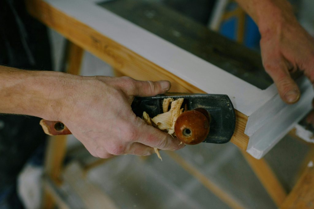 Von oben: Anonymer Schreiner bei der Arbeit beim Zuschneiden eines Holzrahmens mit einem Handhobel.
