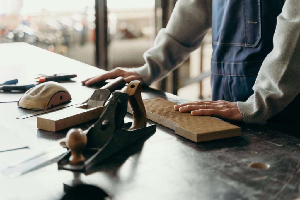 Ein Schreiner arbeitet in einer Industriewerkstatt mit Werkzeugen und Holz an einem Tisch.